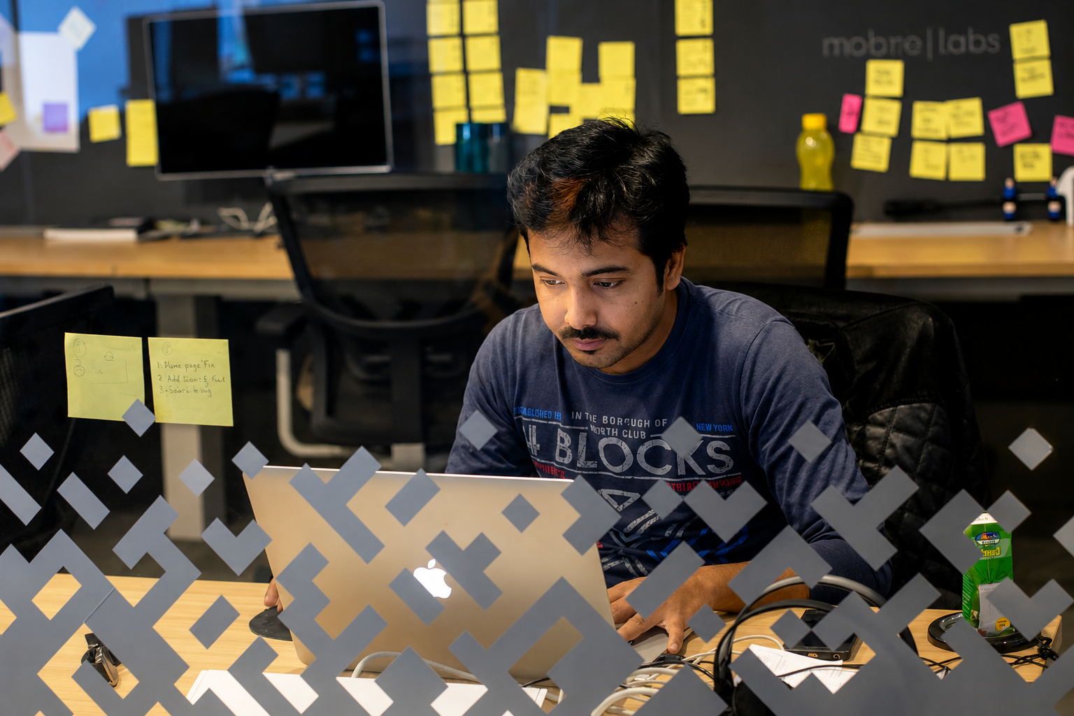 Designer working at his desk, viewed through a glass office partition with sticky notes on the wall